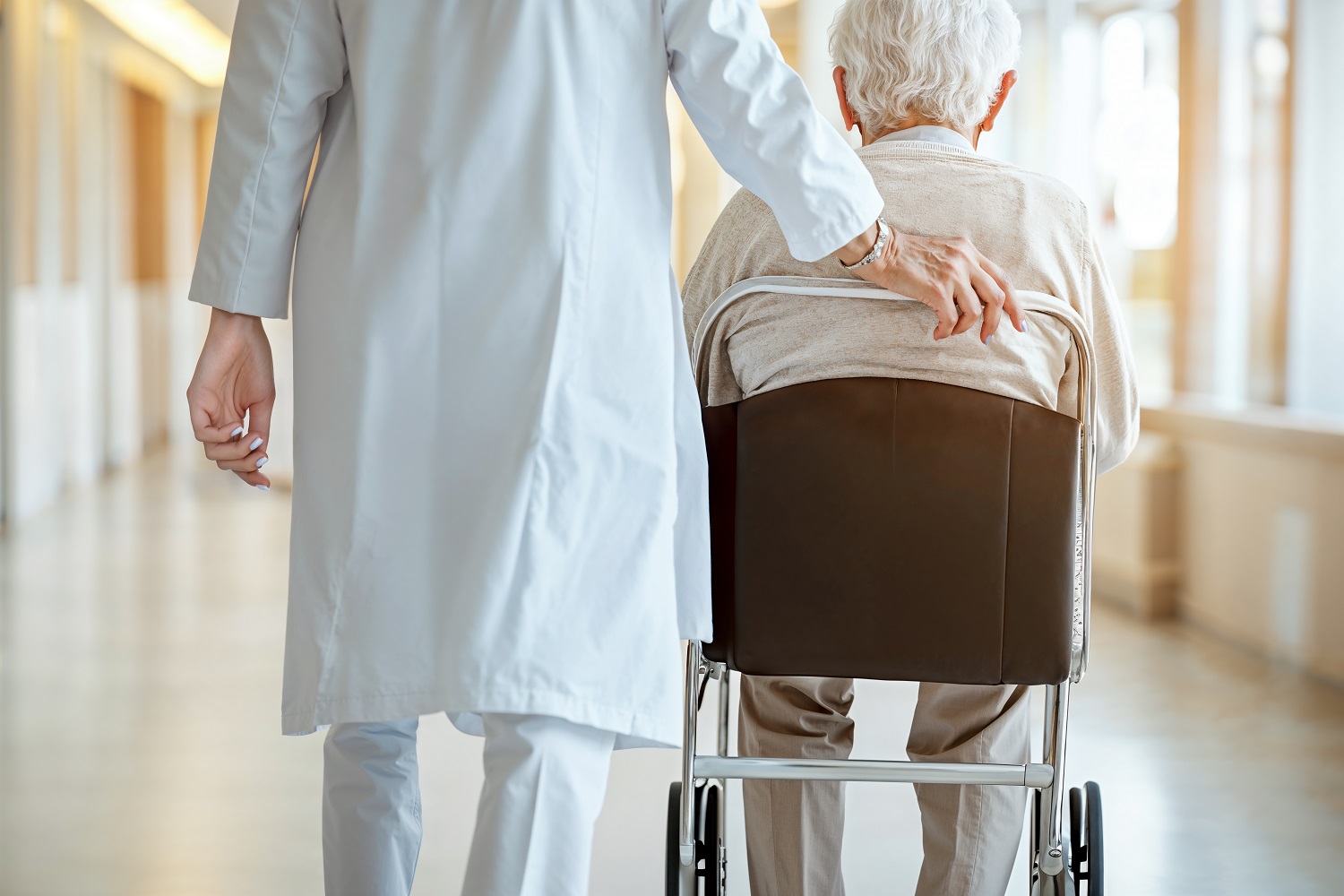 Doctor helps elderly patient in hospital hallway.